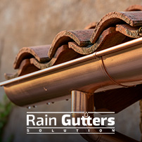 A macro architectural shot showing a custom copper half-round gutter fitted with an extended drip-edge apron tucking neatly beneath the lower edge of Spanish terracotta roof tiles.